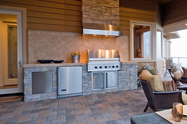 Stone outdoor kitchen with stainless steel appliances and brick paver flooring